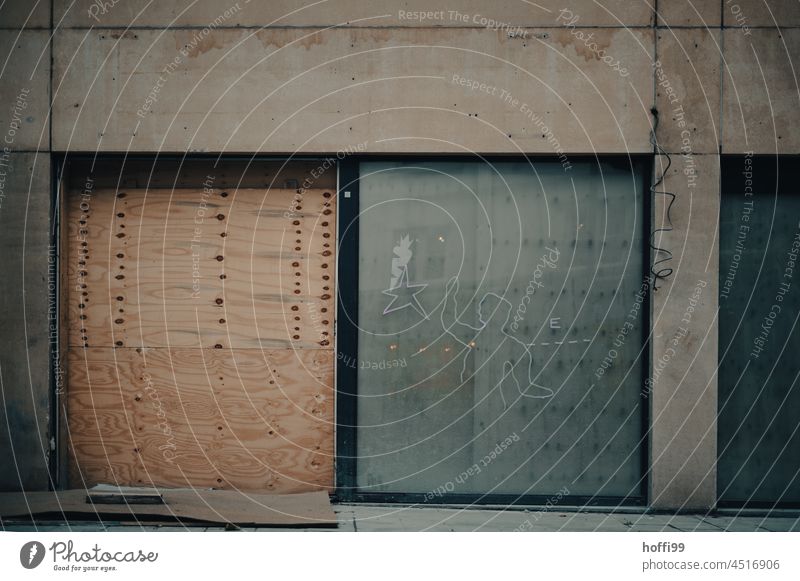 Triste Sichtbetonkonstruktion mit Holz vernageltem Tor und eingesetzter Glasschiebetür - Baustelle Fassade trist grau Beton Architektur Gebäude