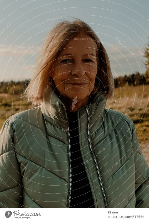 Portrait einer junggebliebenen Rentnerin rente frau ruhestand spazieren zufriedenheit glücklich blond natur landschaft hellblau himmel herbst herbstfarben