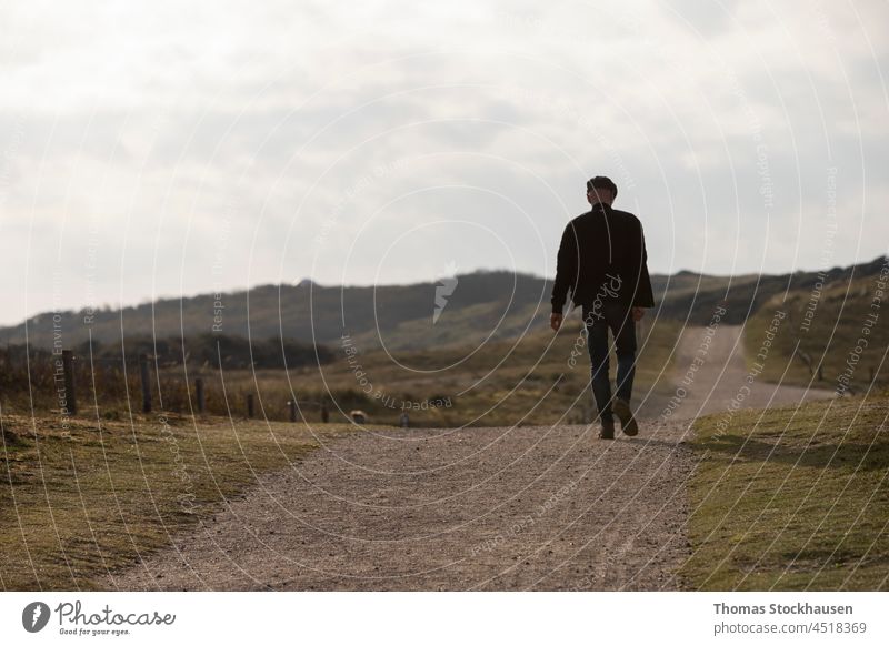 Mann geht auf einem Kiesweg, der zu Dünen führt, bewölkter Himmel im Hintergrund aktiv Erwachsener allein schön Buchse Verschlussdeckel lässig Kaukasier Küste