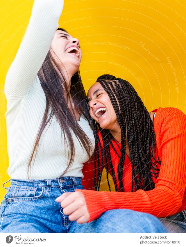 Fröhliche multirassische Frauen lachen vor gelbem Hintergrund Freund Glück Lachen Jeanshose Pullover heiter Freundschaft Stil positiv vielfältig