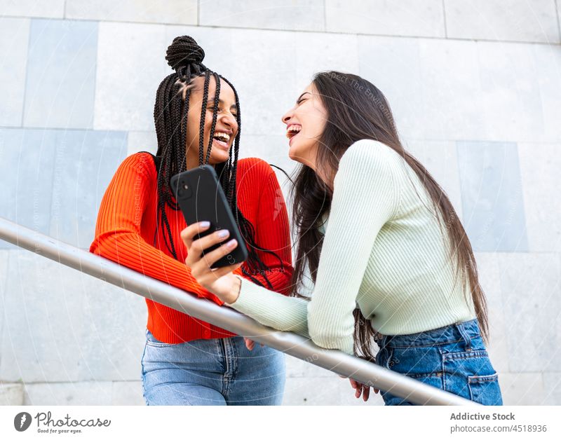 Happy multirassischen Frauen Freunde stehen mit Smartphone in der Nähe von Metall-Geländer Lachen Browsen benutzend Reling heiter Straße Stil trendy Apparatur