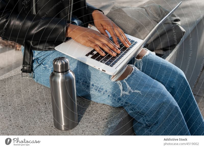 Anonyme schwarze Frau tippt auf einem Laptop Browsen Tippen Straße online freiberuflich Arbeit Notebook modern Netbook Apparatur Computer tragbar Internet