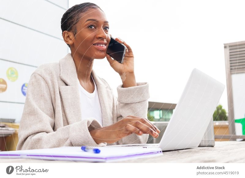 Schwarze Frau spricht in der Nähe eines Laptops mit einem Smartphone Telefonanruf Gespräch diskutieren Straße online freiberuflich Arbeit Netbook Apparatur