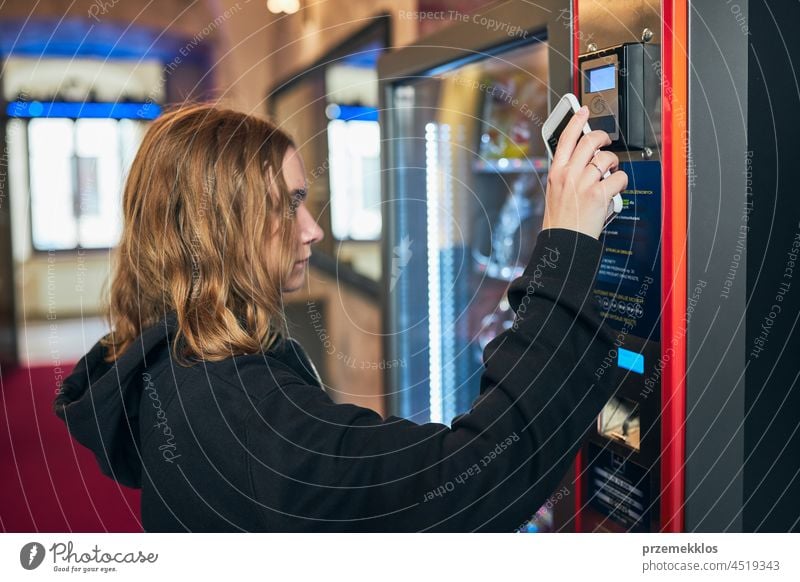Frau, die mit ihrem Smartphone für ein Produkt an einem Verkaufsautomaten bezahlt bezahlen kaufen Verkaufen Maschine berührungslos Zahlung Ware Verbraucher