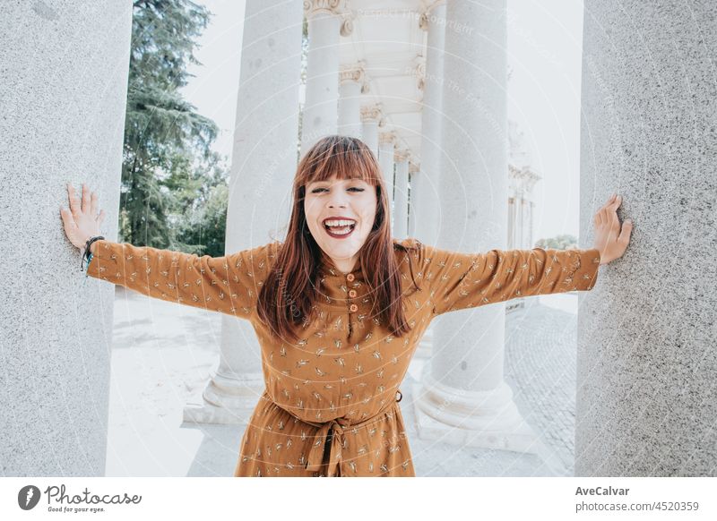 Junge Hipster-Frau in einem herbstlichen Kleid lacht in die Kamera in der Mitte einer alten weißen Säulenkonstruktion, Hipster happy day, Freiheit und Freiheitskonzepte, rothaarige Frau, Social Network Style
