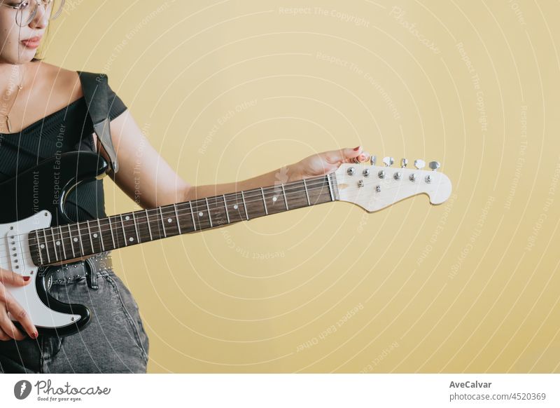 Konzeptuelles Studiobild eines Details einer Frau, die sich bereit macht, eine E-Gitarre zu spielen, gelber Hintergrund, abnehmbarer Hintergrund, Bannerdesign, Werbung in sozialen Netzwerken, Kopierraum