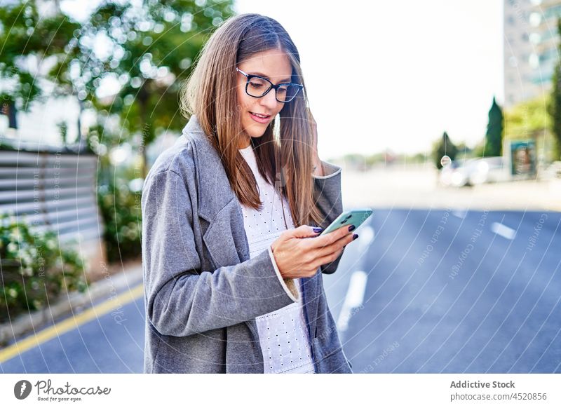 Lächelnde Frau, die beim Gehen auf dem Bürgersteig eine SMS auf ihrem Smartphone schreibt positiv benutzend Nachricht Straße formal Anschluss Internet Großstadt