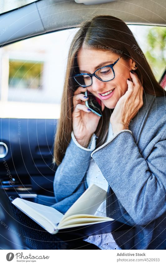 Frau mit Notebook, die im Auto mit ihrem Smartphone spricht Geschäftsfrau PKW benutzend Notizblock Gespräch Arbeit Job zuhören Telefonanruf Unternehmer