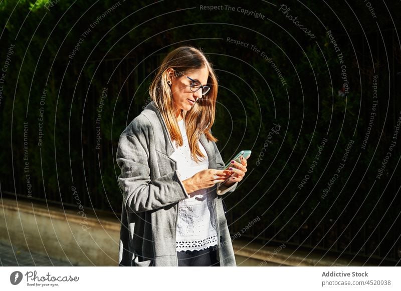 Seriöse Frau benutzt Smartphone auf der Straße prüfen Fokus benutzend Internet zuschauen lesen Arbeit online Nachricht Funktelefon Brille Apparatur
