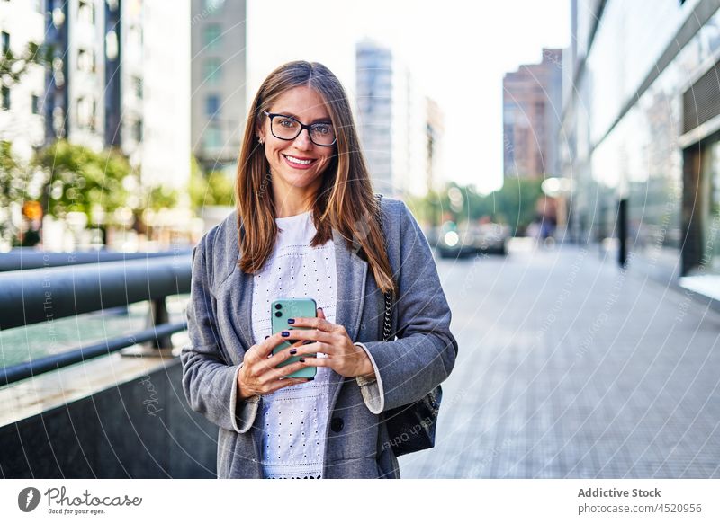 Frau benutzt Smartphone, während sie auf dem Gehweg steht positiv benutzend Nachricht Straße formal Anschluss Internet Großstadt Arbeit professionell