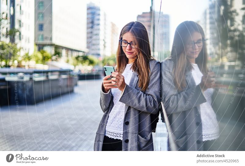 Frau, die auf dem Bürgersteig stehend eine SMS auf ihrem Smartphone schreibt positiv benutzend Nachricht Straße formal Anschluss Internet Großstadt Arbeit