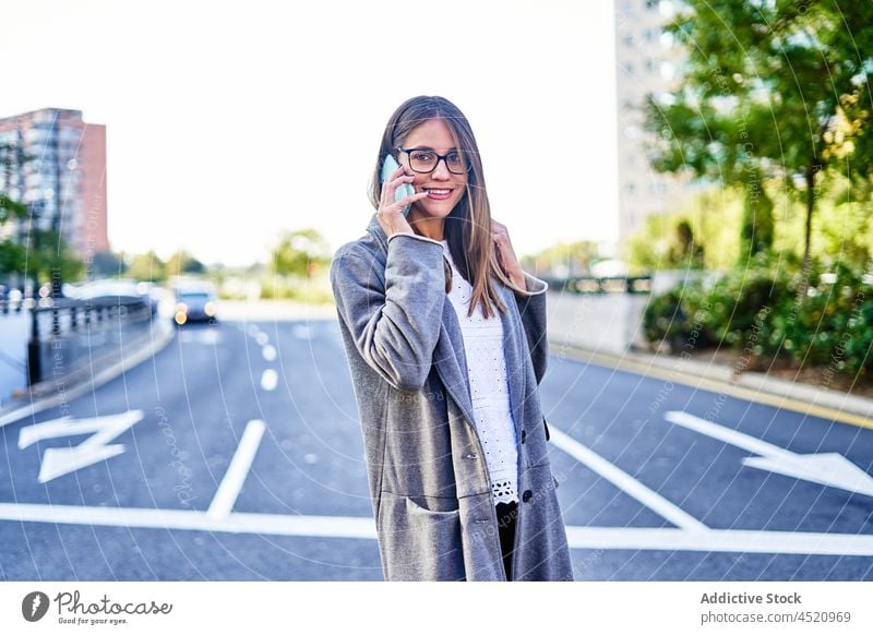 Lächelnde Geschäftsfrau, die mit ihrem Smartphone spricht, während sie die Straße überquert Frau Unternehmer benutzend Telefonanruf positiv formal Gespräch