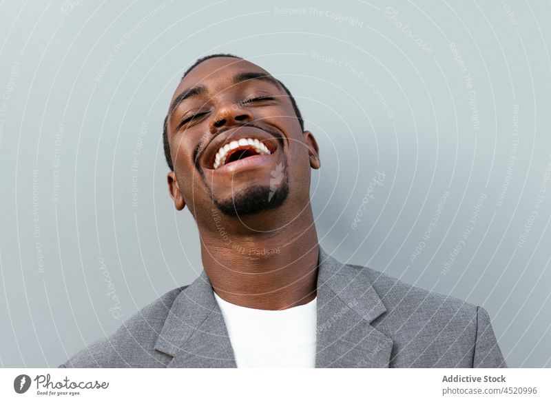 Positiver schwarzer Mann in formellem Outfit steht in der Nähe einer grauen Wand Geschäftsmann positiv formal elegant Lachen respektabel Porträt professionell
