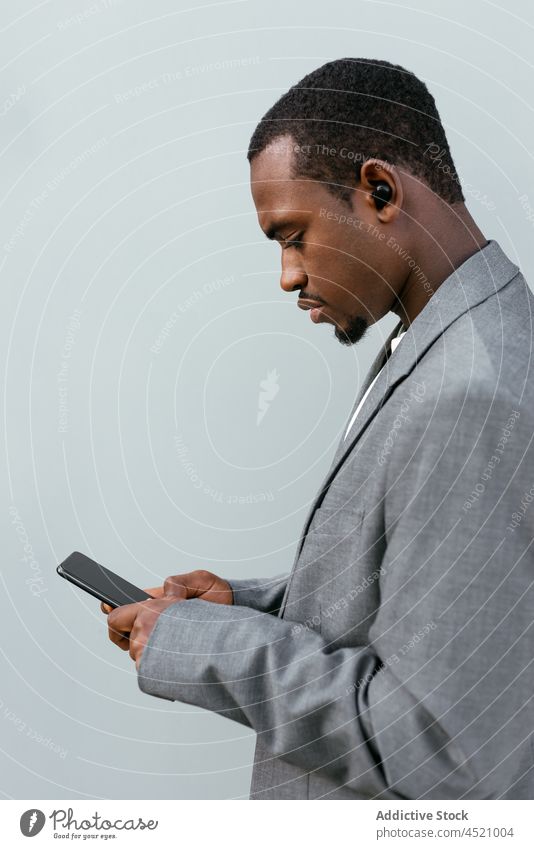 Schwarzer leitender Angestellter, der auf seinem Smartphone surft Geschäftsmann benutzend formal Anschluss online Anzug Browsen zuhören Musik Ohrstöpsel Mann