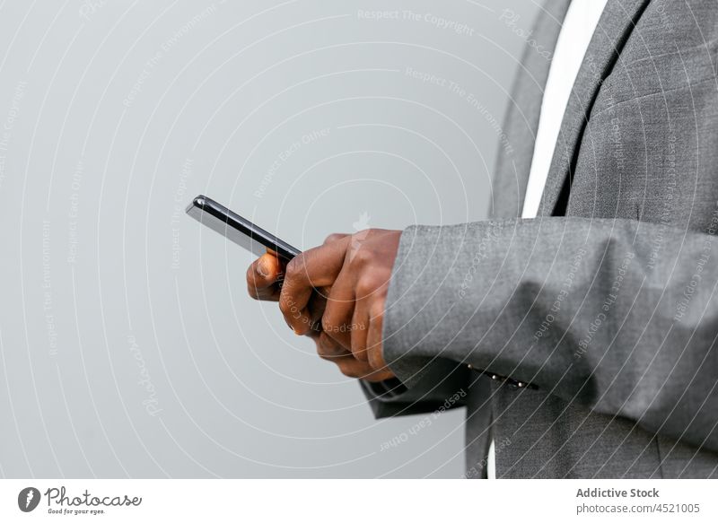 Schwarzer leitender Angestellter, der auf seinem Smartphone surft Geschäftsmann benutzend formal Anschluss online Anzug Browsen zuhören Musik Mann männlich