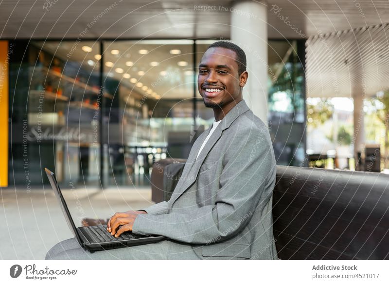 Schwarzer Geschäftsmann tippt auf Laptop auf einer Straßenbank Tippen benutzend online Arbeit Inbetriebnahme Projekt Mann Unternehmer Fokus Netbook Gerät