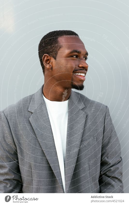 Positiver schwarzer Mann in formellem Outfit steht in der Nähe einer grauen Wand Geschäftsmann positiv formal elegant respektabel Porträt professionell