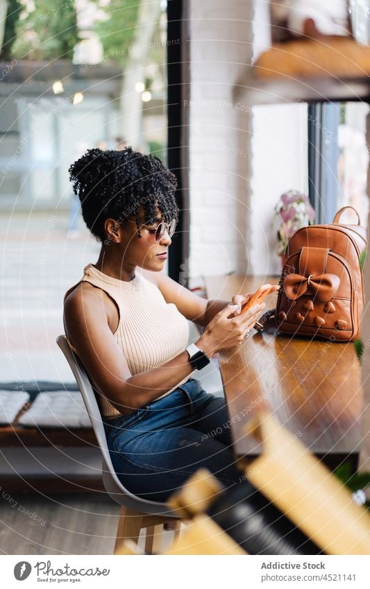 Seriöse stilvolle schwarze Dame mit Smartphone im Café Frau benutzend trendy selbstbewusst Kommunizieren online Freizeit Nachricht soziale Netzwerke Stil