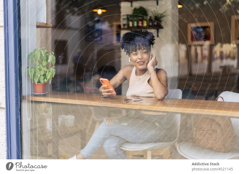 Fröhliche schwarze Frau während eines Videogesprächs per Smartphone in der Cafeteria Videoanruf heiter Kommunizieren Café Gespräch reden Freude Fenster jung