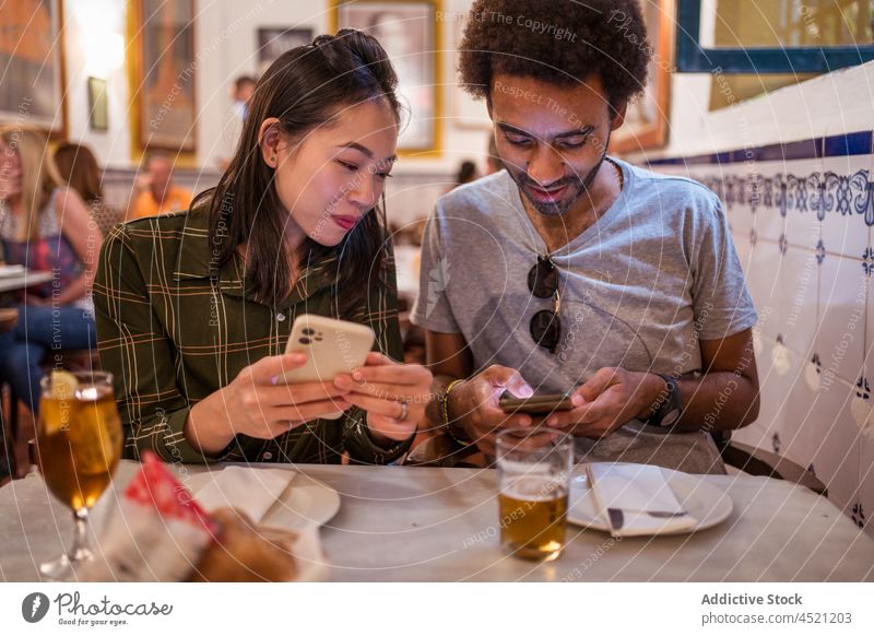 Positives junges gemischtes Paar, das sich im Restaurant Smartphones teilt benutzend positiv Termin & Datum Bier Zusammensein soziale Netzwerke Glück