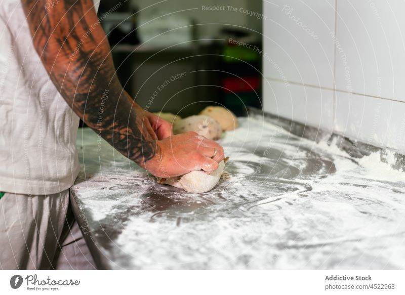 Junger Mann rollt Teig in der Bäckereiküche kneten Teigwaren Küche Brot vorbereiten Abfertigungsschalter Arbeit Gebäck Kleinunternehmen männlich jung Tattoo