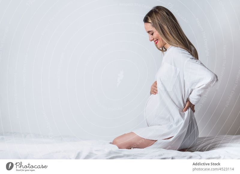 Positive schwangere Frau mit Hand auf dem Rücken auf dem Bett sitzend Bauch Angebot sanft mütterlich Harmonie positiv vorwegnehmen erwarten Schwangerschaft
