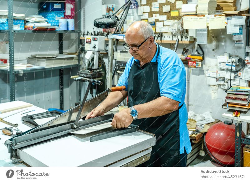 Ernster älterer männlicher Meister an einer Schneidemaschine in einer Werkstatt Mann geschnitten Schachtel drucken Kunstgewerbler Prozess Maschine Konzentration