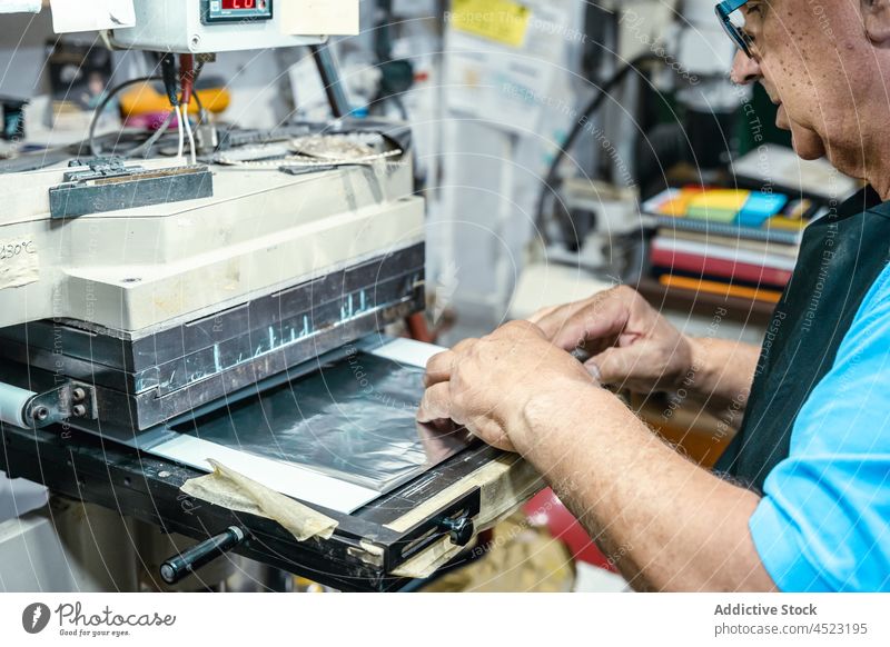 Älterer Handwerker bei der Arbeit mit einer Laminiermaschine in einer Druckerei Mann arbeiten Maschine Lamellierung drucken Druckmaschine achtsam Kunstgewerbler