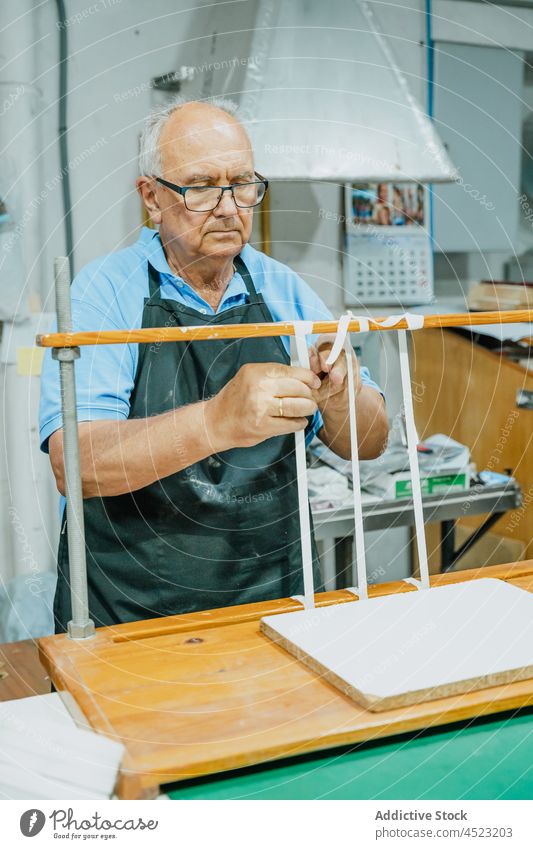Fokussierter älterer männlicher Handwerker beim Binden von Bändern auf einem Holzbrett im Druckatelier Mann Krawatte Klebeband drucken Druckmaschine Arbeit
