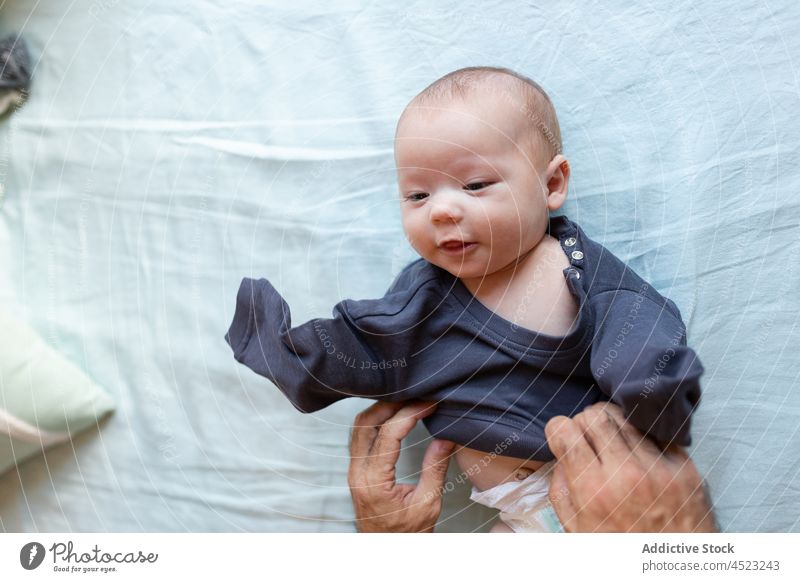 Crop Dad Dressing Neugeborenen auf dem Bett Baby Mann Vater angezogen Streicheln Kinderbetreuung Schlafzimmer Lügen unschuldig Pflege Elternschaft niedlich
