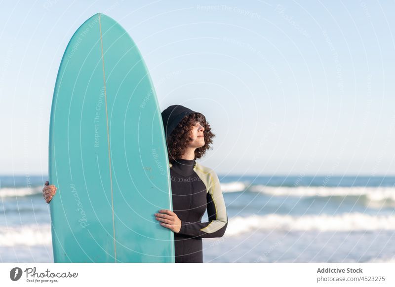 Lockenköpfige Frau mit Surfbrett am Meeresufer Surfer MEER tropisch Strand winken schäumen sorgenfrei Aktivität Neoprenanzug Brandung Küste Ufer Wasser