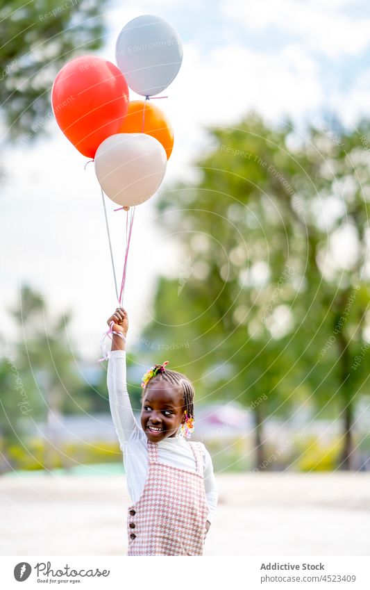 Glückliches schwarzes Mädchen läuft mit bunten Luftballons laufen heiter Kind Lächeln Stil positiv Park Afroamerikaner ethnisch farbenfroh Outfit Spaß hell