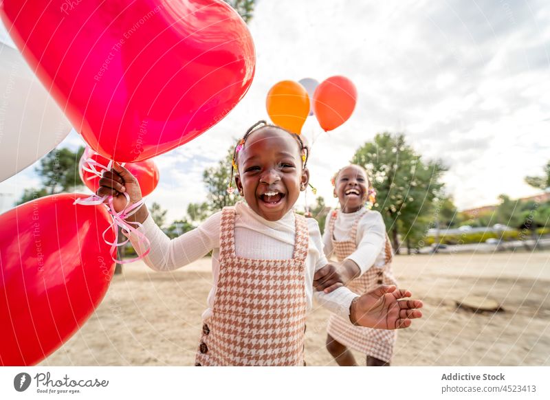 Positive schwarze Mädchen mit Luftballons stehen auf Gras im Park Kinder Lächeln Glück Schwester Kleid positiv Freude Afroamerikaner wenig ähnlich ethnisch