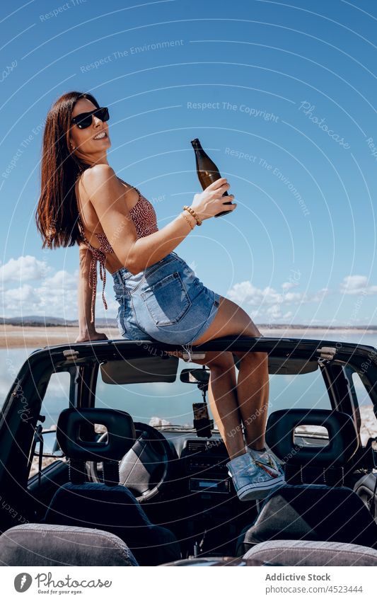 Fröhliche Frau sitzt mit einer Bierflasche auf einem Auto PKW Safari Glück Flasche Fluss Kälte cool Freiheit Abenteuer sorgenfrei Sonnenbrille