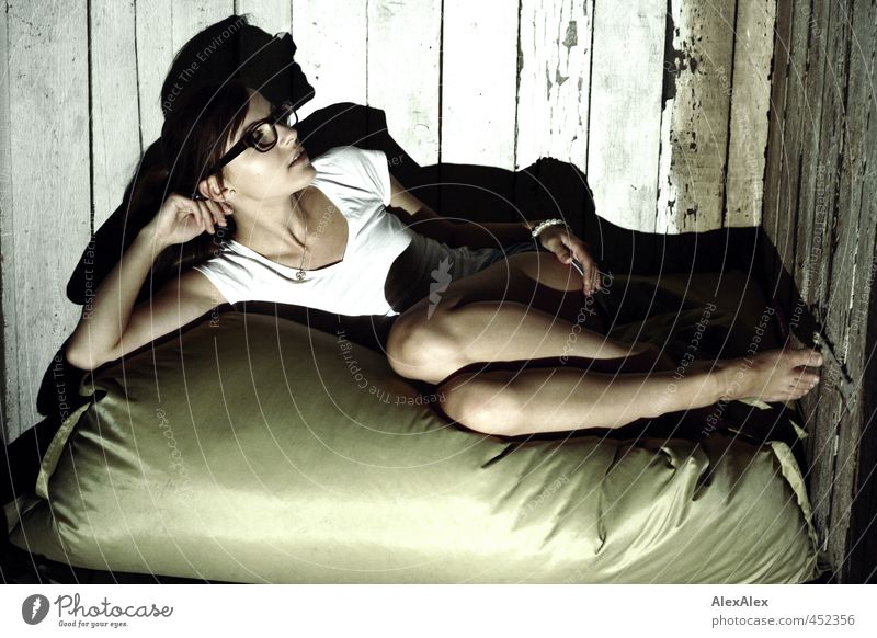 Junge, barfüßige Frau liegt auf Sitzkissen vor einer Bretterwand Junge Frau Jugendliche Körper Beine 18-30 Jahre Erwachsene T-Shirt Brille Barfuß Holz Denken