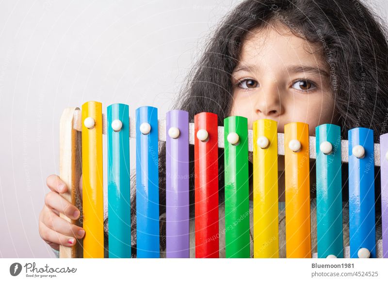 Porträt eines kleinen Mädchens mit Xylophon in der Hand, das ausdrucksvoll in die Kamera schaut, Kindheitserinnerungen vier Jahre Musik Werkzeuge farbenfroh