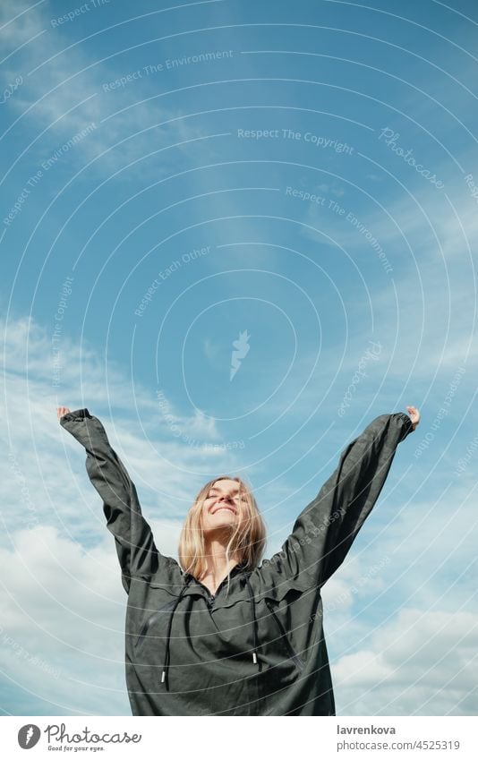 Junge blonde Frau in khakifarbenem Hemd mit erhobenen Händen vor blauem Himmel im Freien khakigrün hübsch vertikal Landschaft Sommer Entdecker Freiheit Wind