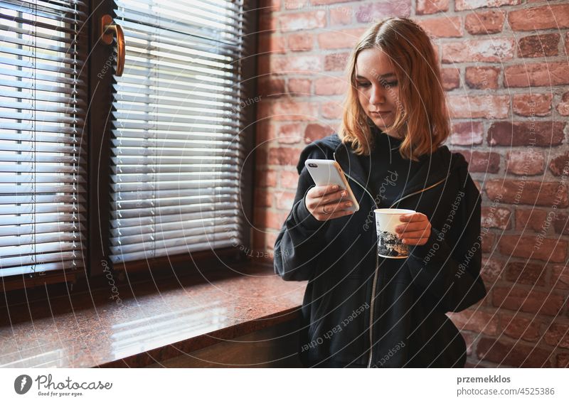 Frau schreibt eine SMS auf ihrem Smartphone und trinkt Kaffee, während sie eine Pause im Büro macht benutzend Texten Mobile Telefon trinken Person