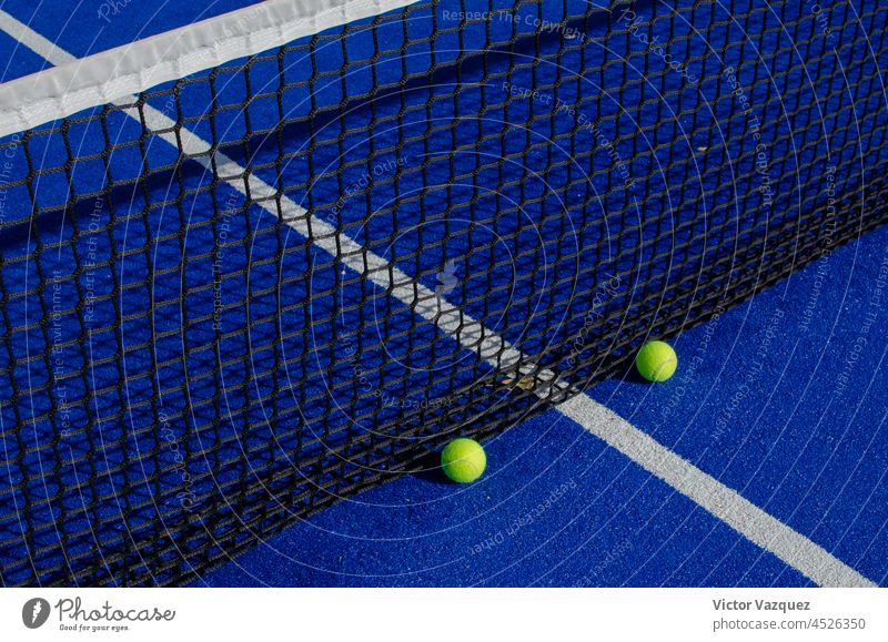 Zwei Bälle neben dem Netz eines blauen Paddle-Tennisplatzes. Schatten Padelplatz Gerichte Padel-Tennis Textur Boden Stillleben Rasen Kunstrasen Leichtathletik