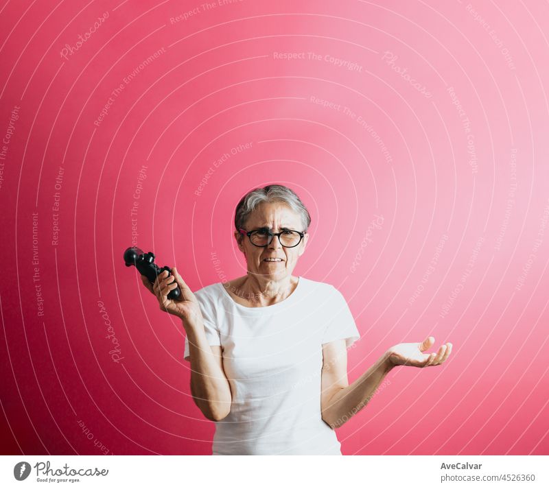 Alte ältere Frau verwirrt, während eine Konsole Pad, Videospiele spielen Pastell rosa abnehmbaren Hintergrund, Videospiele alte Menschen, Kopie Raum, weißes Hemd Raum