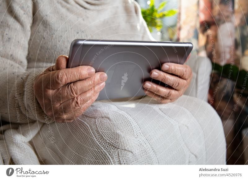 Nahaufnahme faltige Hände einer alten Frau mit Tablet-Computer. Ältere Dame sitzt im Stuhl mit Decke. Warm und gemütlich, Zeit zum Entspannen, Surfen, Film schauen.