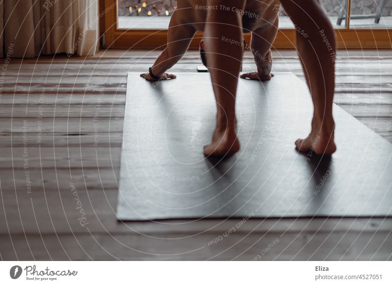 Ein Mann macht zuhause mit einem Kurs auf seinem Handy Yogaübungen auf einer Yogamatte yogaübung Zuhause nackt Lifestyle Telefon Fitness Holzboden schwarz