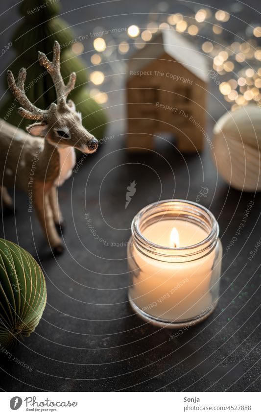 Eine brennende Kerze im Glas und Weihnachtsdekoration auf einem schwarzen Tisch Lichterkette Weihnachten & Advent Reh Dekoration & Verzierung Christbaumkugel