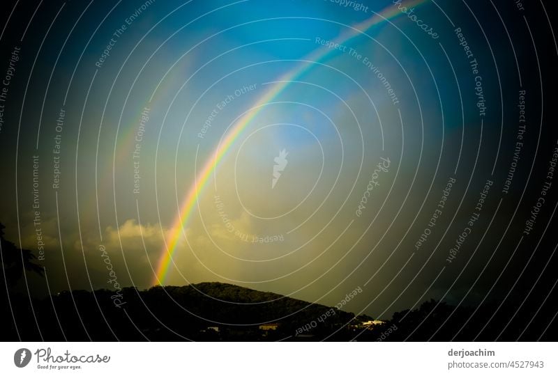 Nach einem Regenschauer,  erscheint ein  wunderschönes  Regenbogen Spektakel,  auf den Hügeln . Ein kleines Stück vom blauen Himmel ist auch schon zu sehen.