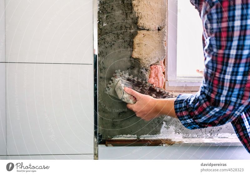 Maurerin beim Nivellieren von Zement mit einer Glättkelle unkenntlich Hand Kelle Niveau Beton Wandfliese Bad Nahaufnahme Maurerhandwerk Textfreiraum