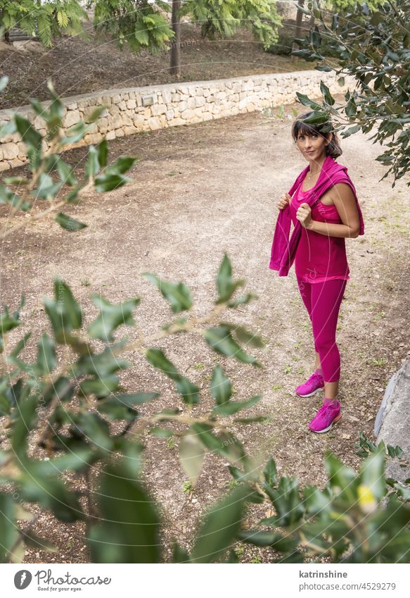 Lächelnde Frau in rosa Sportkleidung in einem Park Sportbekleidung Aufenthalt Glück allein Gesundheit Sommer grün mittleres Alter reif im Freien Fitness