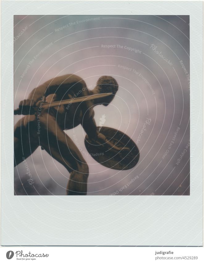Vergoldete Skulptur eines Kriegers auf Polaroid Kämpfer Mann kämpfen Waffe Kraft Soldat Schlacht Schild Schwert Gefecht Licht unheimlich Himmel Dynamik