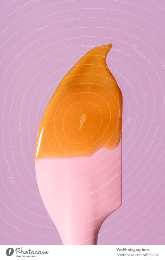 Karamellsauce, die auf einen Silikonspatel tropft, minimalistisch auf einem rosa Hintergrund. backen braun Kalorien Weihnachten Nahaufnahme Farbe kondensiert