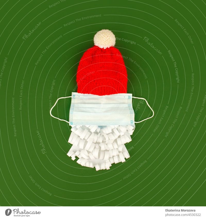 Weihnachtsmann-Mütze und Papier-Bart mit medizinischen Gesichtsmaske auf klassischen grünen Hintergrund, kreative minimale Konzept von Weihnachten und Neujahr 2022, covid-19 Lockdown, neue Normalität