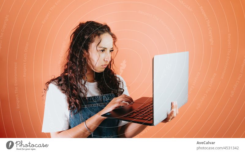 Junge gemischtrassige Frau hält einen Laptop und ist besorgt über etwas, das sie auf dem Bildschirm sieht, orangefarbener Hintergrund, abnehmbarer Hintergrund, minimales Bild, Kopierraum, Grundsituationen